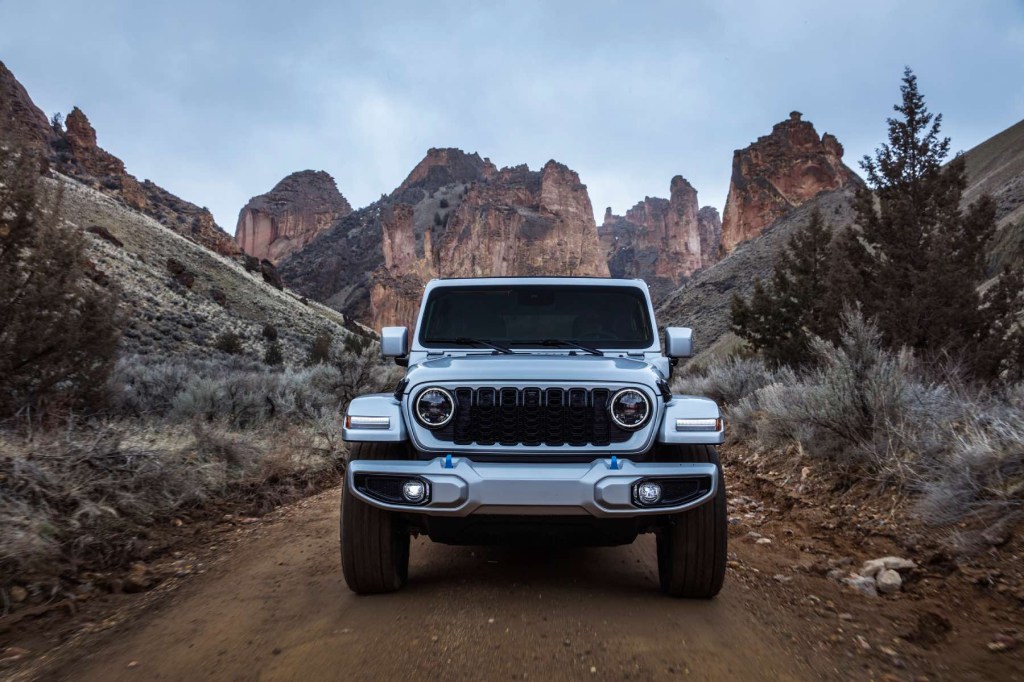 A Wrangler 4xe drives on a trail with a dramatic desert mountain scenery in the background. Jeep claims a Wrangler EV is on the way in years ahead.