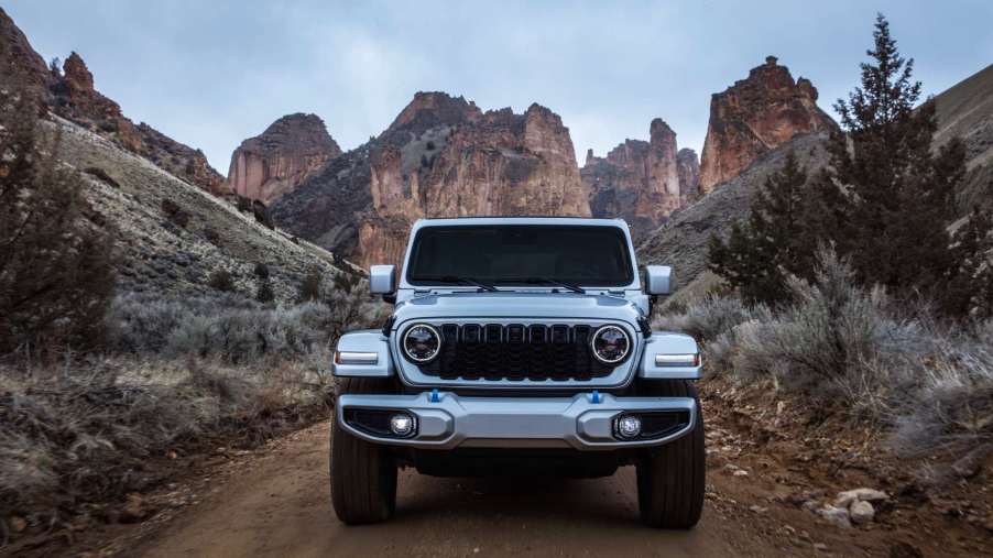 A Wrangler 4xe drives on a trail with a dramatic desert mountain scenery in the background. Jeep claims a Wrangler EV is on the way in years ahead.