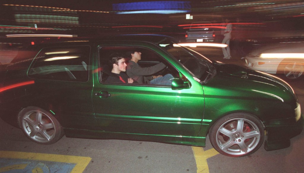 A green Volkswagen hatchback drives to a car meet