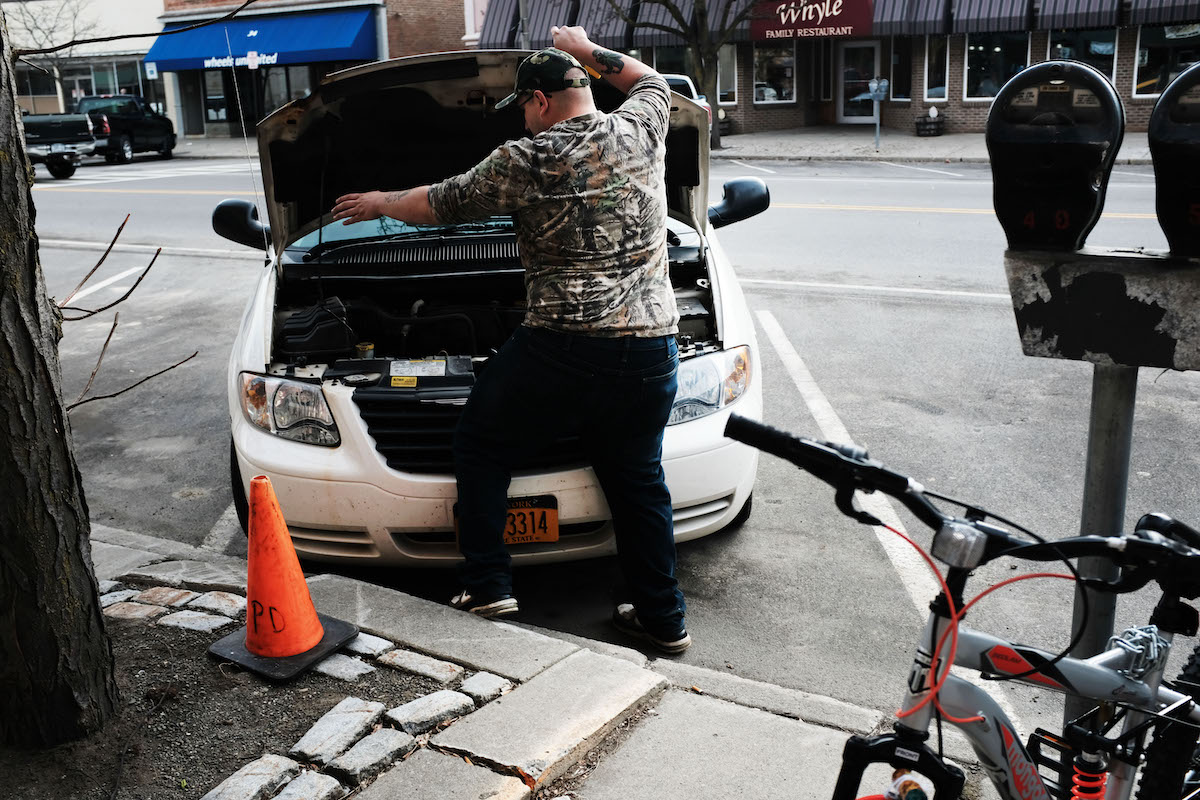 Man looking un the hood of his broken down car. What car sounds happened to make this problem?