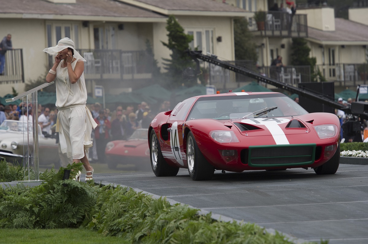 A presenter covers her ears as a 1966 Ford GT40 mark 1 drives over the ramp during the 2013 Pebble Beach Concours d' Elegance in Pebble Beach, California, U.S., on Sunday, Aug. 18, 2013. The annual event in its 63rd year raised $1.277 million U.S. dollars for charity and showcased 248 cars, 48 from abroad. Photographer: David Paul Morris/Bloomberg via Getty Images