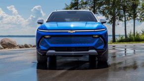 A blue 2024 Chevy Equinox EV 3LT compact electric SUV model parked on wet pavement near water