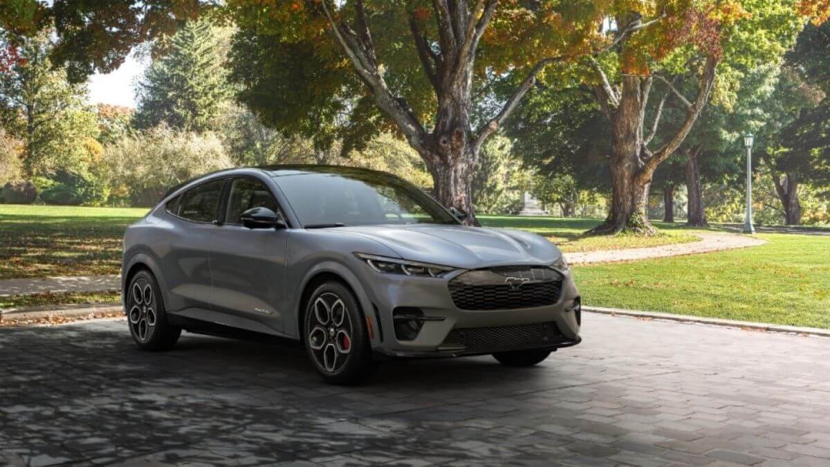 A 2023 Ford Mustang Mach-E compact EV SUV model parked on a cobblestone path under the shade of a tree