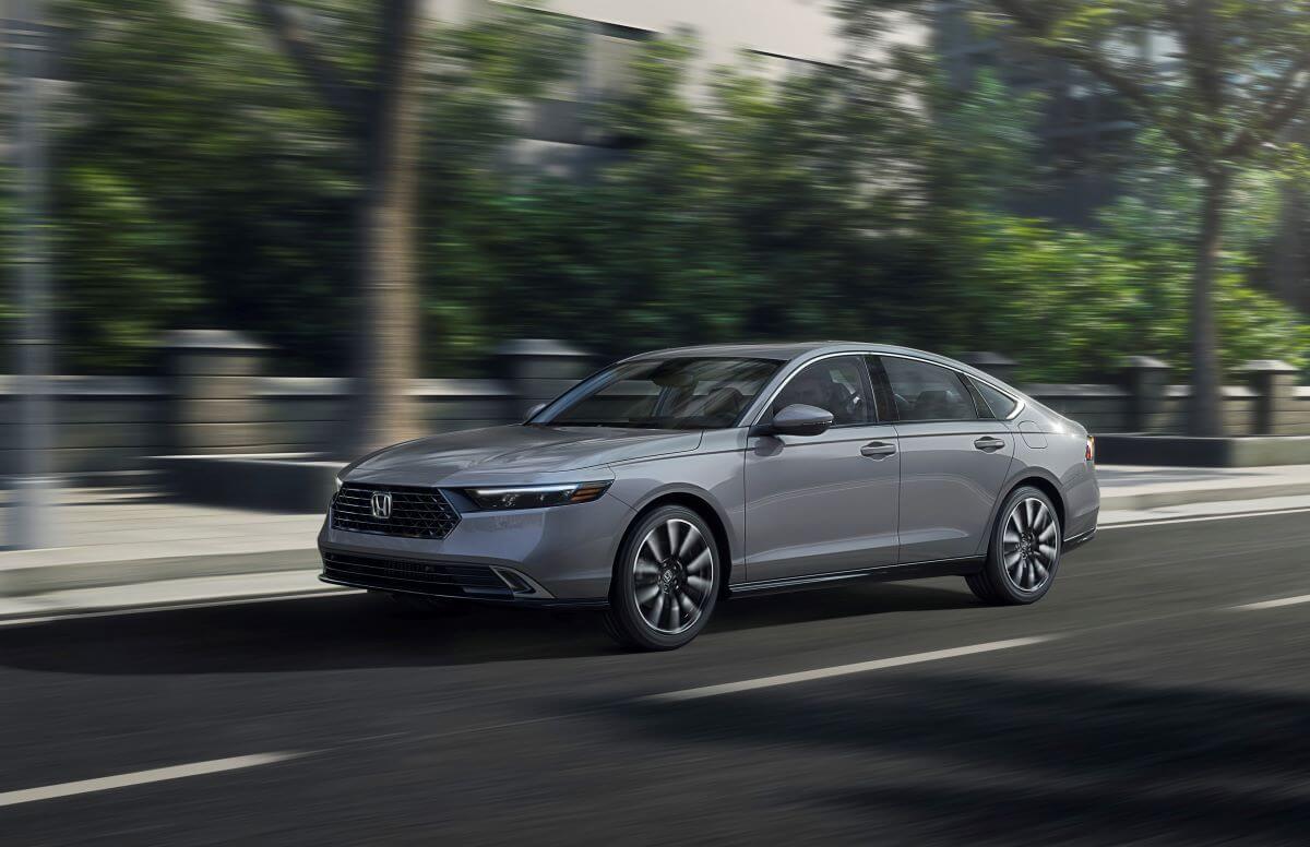 A gray 2023 Honda Accord Touring midsize sedan model driving past a park with a blurred background