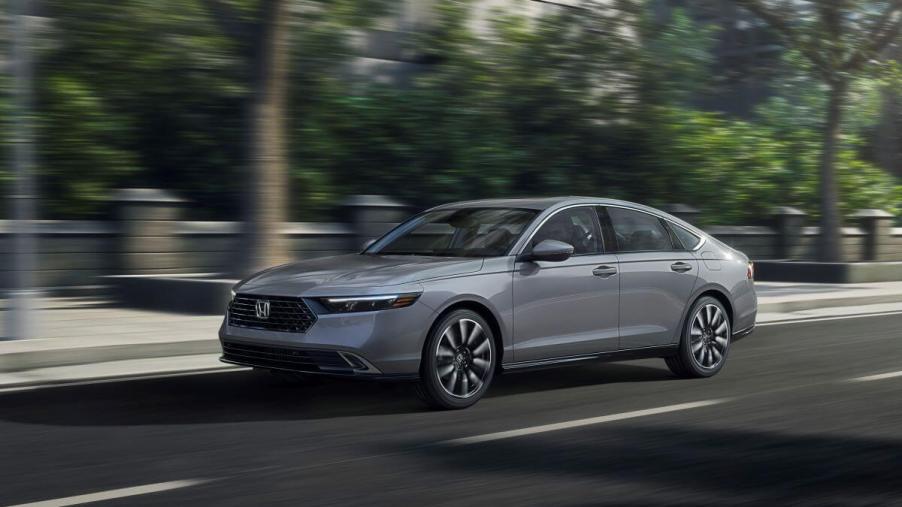 A gray 2023 Honda Accord Touring midsize sedan model driving past a park with a blurred background.