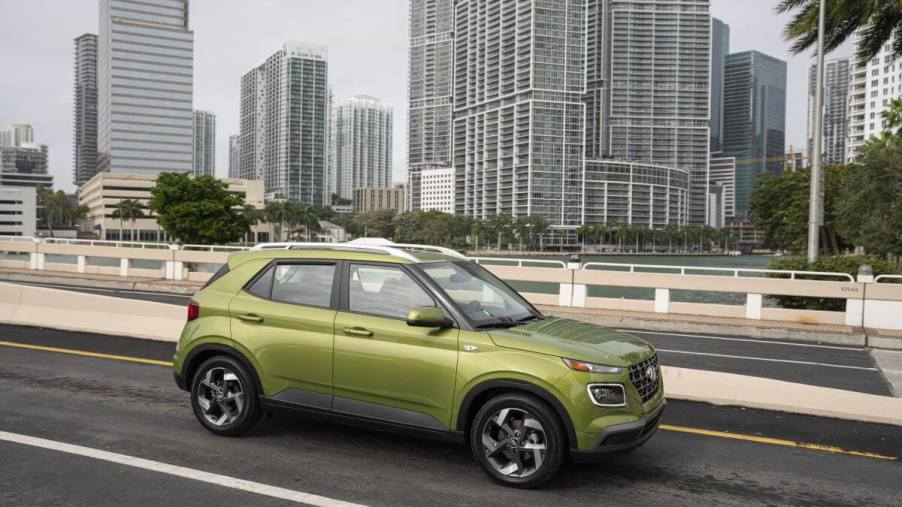 A bright green 2023 Hyundai Venue subcompact SUV model parked on a highway overpass with skyscrapers behind it