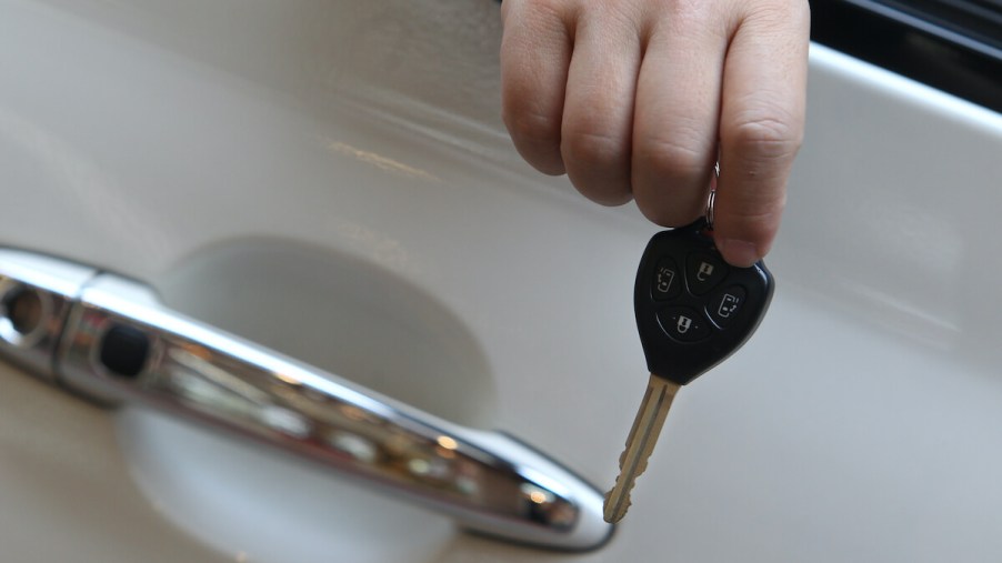 A man's hand holds a car key out a car door window.