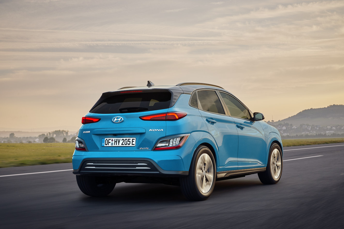 The rear of a blue 2023 Hyundai Kona Electric driving into the sunset