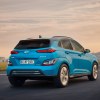 The rear of a blue 2023 Hyundai Kona Electric driving into the sunset