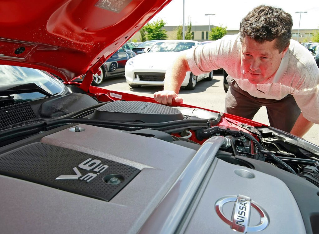A sales manager at a dealership inspects the engine on a Nissan 350Z