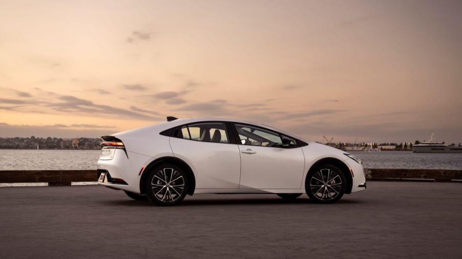A side profile shot of a 2023 Toyota Prius hybrid hatchback model in Wind Chill Pearl parked by the sea
