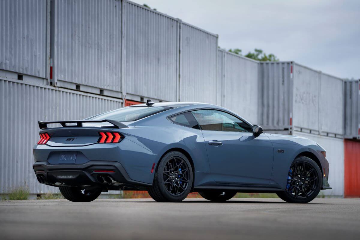 A rear exterior side shot of a blue-gray 2024 Ford Mustang muscle car coupe model parked near shipping containers