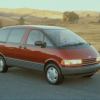 A red 1991 Toyota Previa minivan model parked on the side of a road near fields of yellow grass