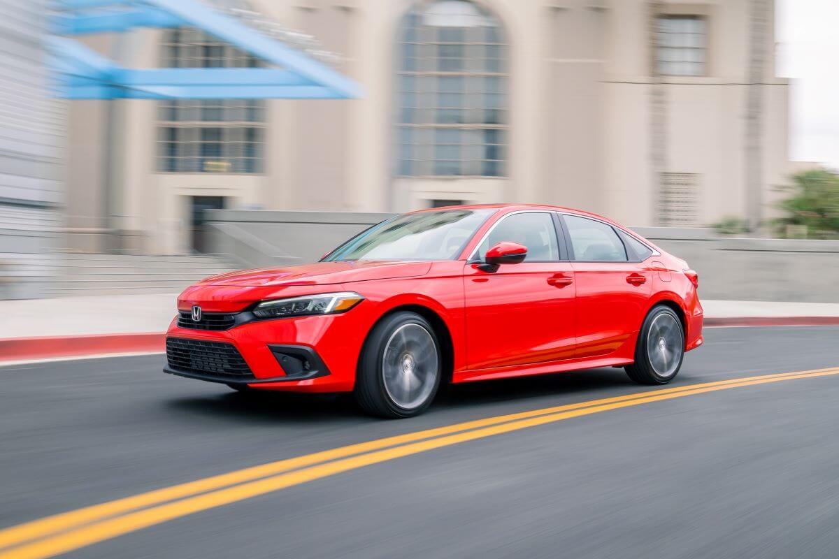 A bright red 2023 Honda Civic compact sedan model speeding past a building entrance with a blurred background