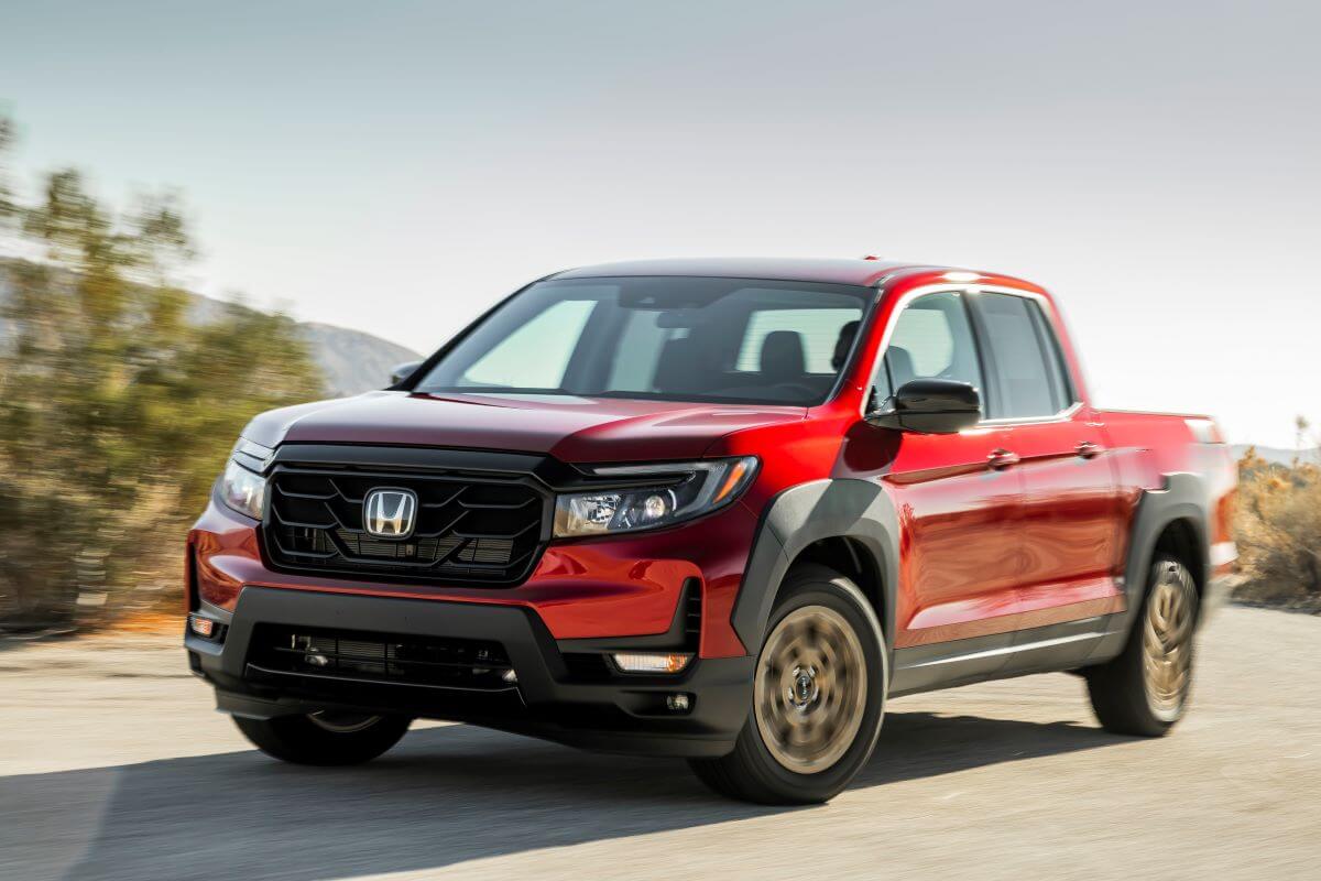 A red 2023 Honda Ridgeline Sport midsize pickup truck model with HPD Package driving in the desert