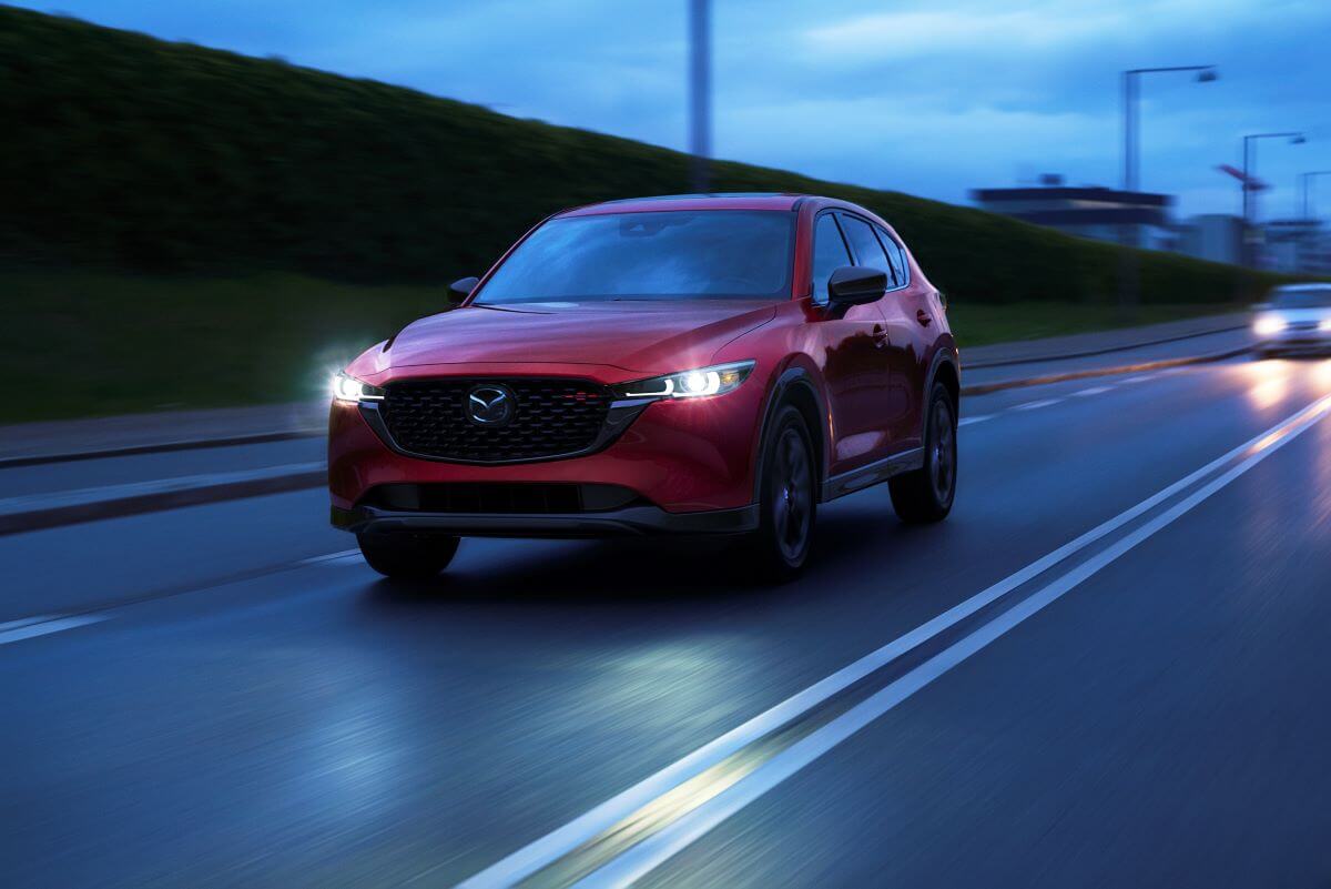 A red 2023 Mazda CX-5 compact SUV model driving at night with its headlights on