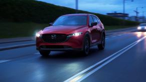 A red 2023 Mazda CX-5 compact SUV model driving at night with its headlights on