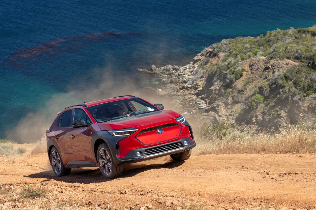 A red 2023 Subaru Solterra EV with AWD driving up a sand and gravel hill as it kicks up dust