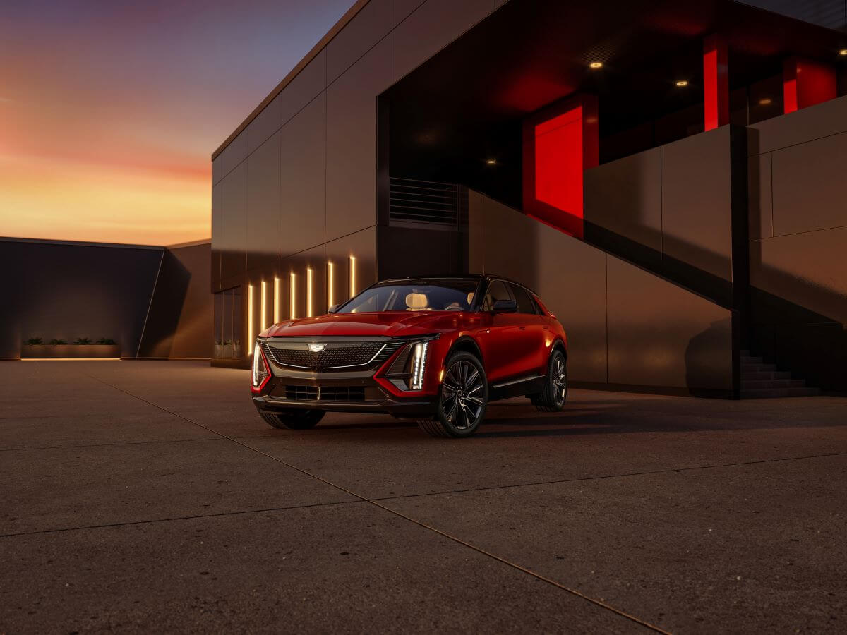A red 2024 Cadillac Lyriq electric full-size luxury SUV model parked outside a luxury building at sunset