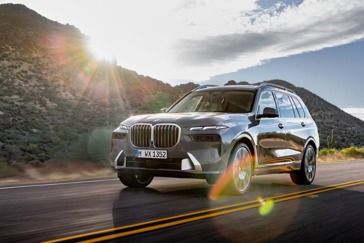 A gray 2023 BMW X7 on the road with a mountain and the sun in the background