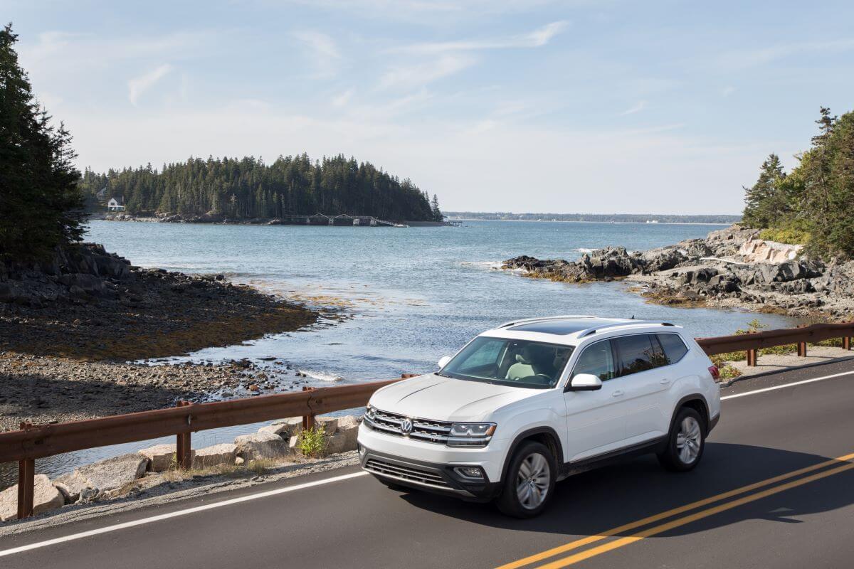 A white 2018 Volkswagen Atlas midsize, three-row SUV model crossing a bridge near forest trees and lakes