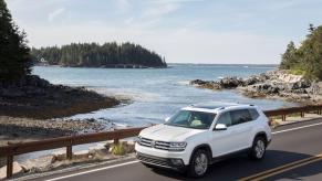 A white 2018 Volkswagen Atlas midsize, three-row SUV model crossing a bridge near forest trees and lakes