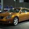 A yellow 2004 Nissan Maxima full-size sedan model on display at the 2003 North American International Auto Show