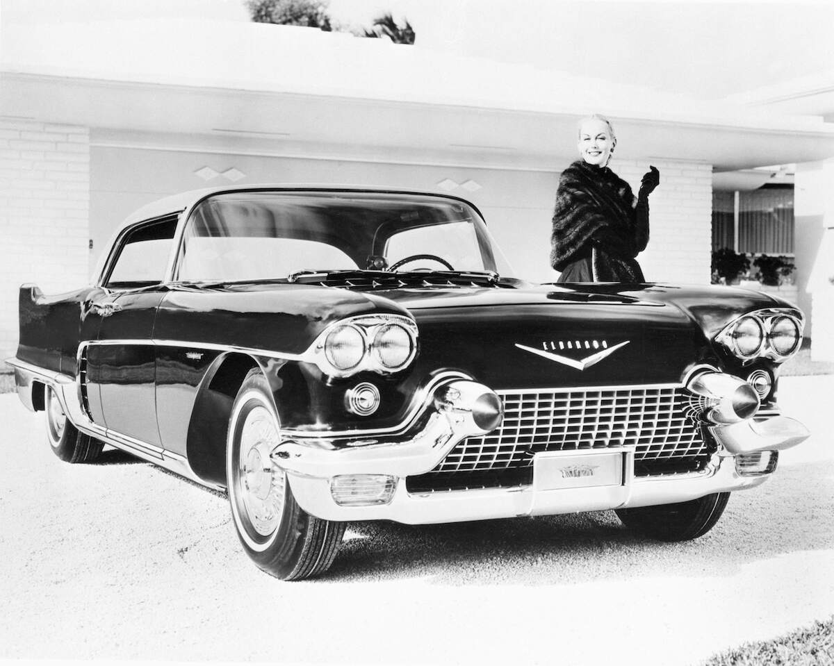 A smiling woman stands beside a 1957 Cadillac Eldorado Brougham