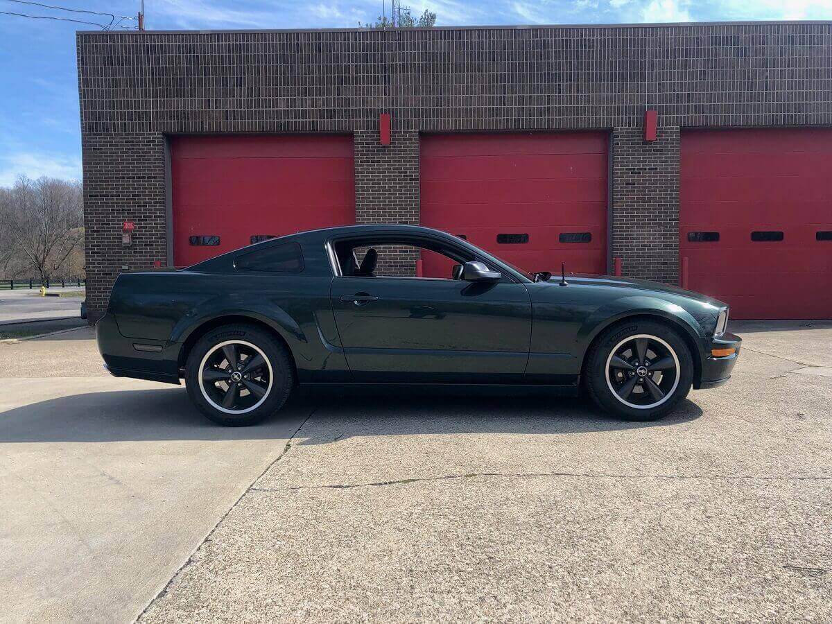 A Mustang Bullitt shows off its rear-end styling in front of a garage door.