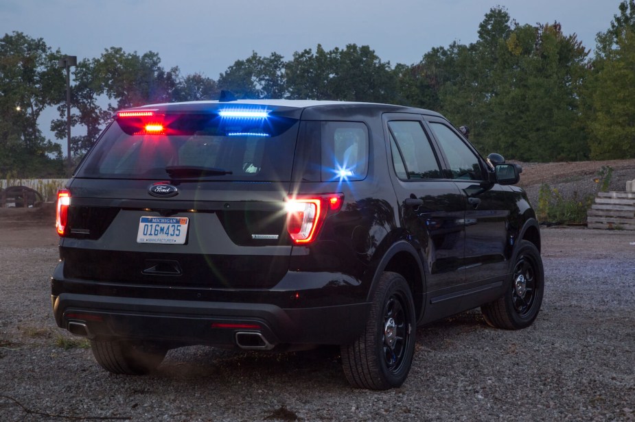 The back of an unmarked Ford Interceptor police cruiser car parked in a gravel lot, trees visible in the bakcground.