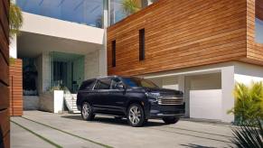 A 2023 Chevy Suburban High Country full-size SUV model parked outside the garage of a wood and brick complex