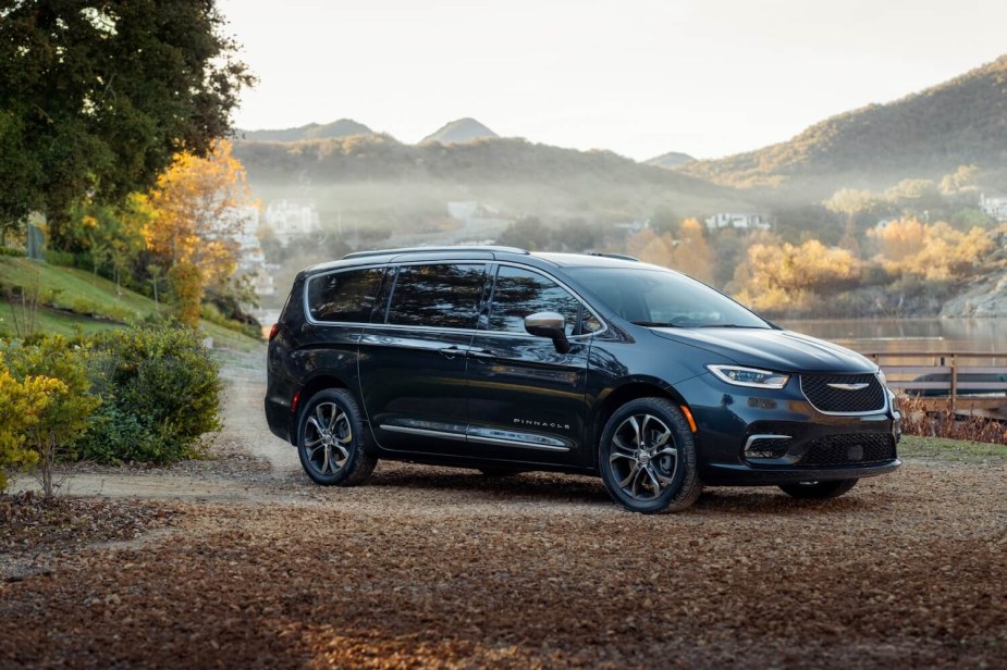 A dark gray Chrysler Pacifica PHEV minivan parked in front of a mountain range with orange foliage.