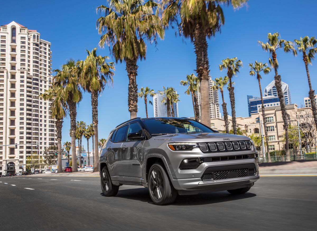 A 2023 Jeep Compass High Altitude compact SUV model driving under palm trees