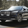 A 2023 Lincoln Aviator midsize luxury SUV model driving on a forest highway road