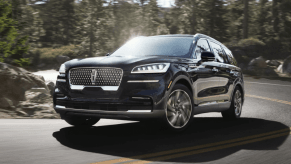 A 2023 Lincoln Aviator midsize luxury SUV model driving on a forest highway road