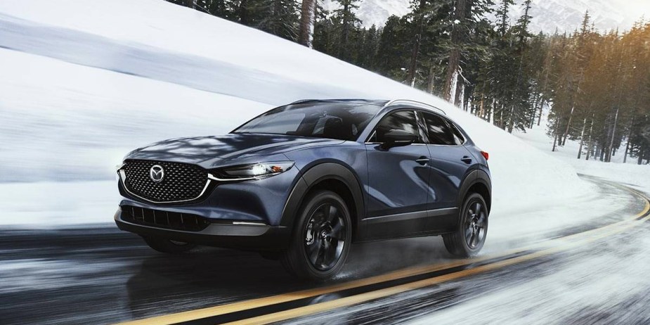 A blue 2023 Mazda CX-30 subcompact SUV is driving on a wet road. 