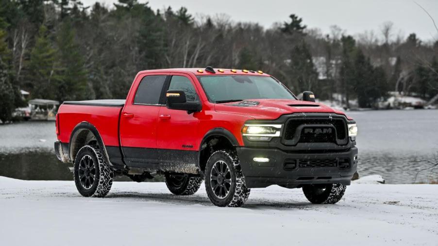 A red 2023 Ram 2500 Heavy Duty Rebel pickup truck model parked in the snow near a forest and frozen lake