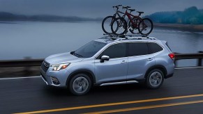 A blue 2023 Subaru Forester small SUV is driving on the road.