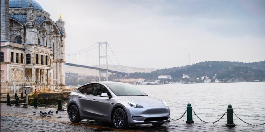 A gray 2023 Tesla Model Y small electric SUV is parked near the water. 