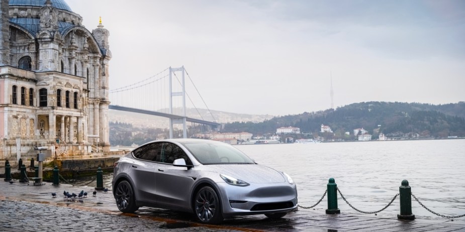 A gray 2023 Tesla Model Y small electric SUV is parked near water. 