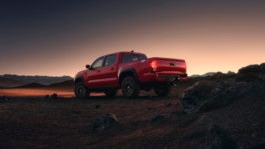 The back of a red 2023 Toyota Tacoma manual transmission pickup truck parked off-road, the sunset visible in the background.