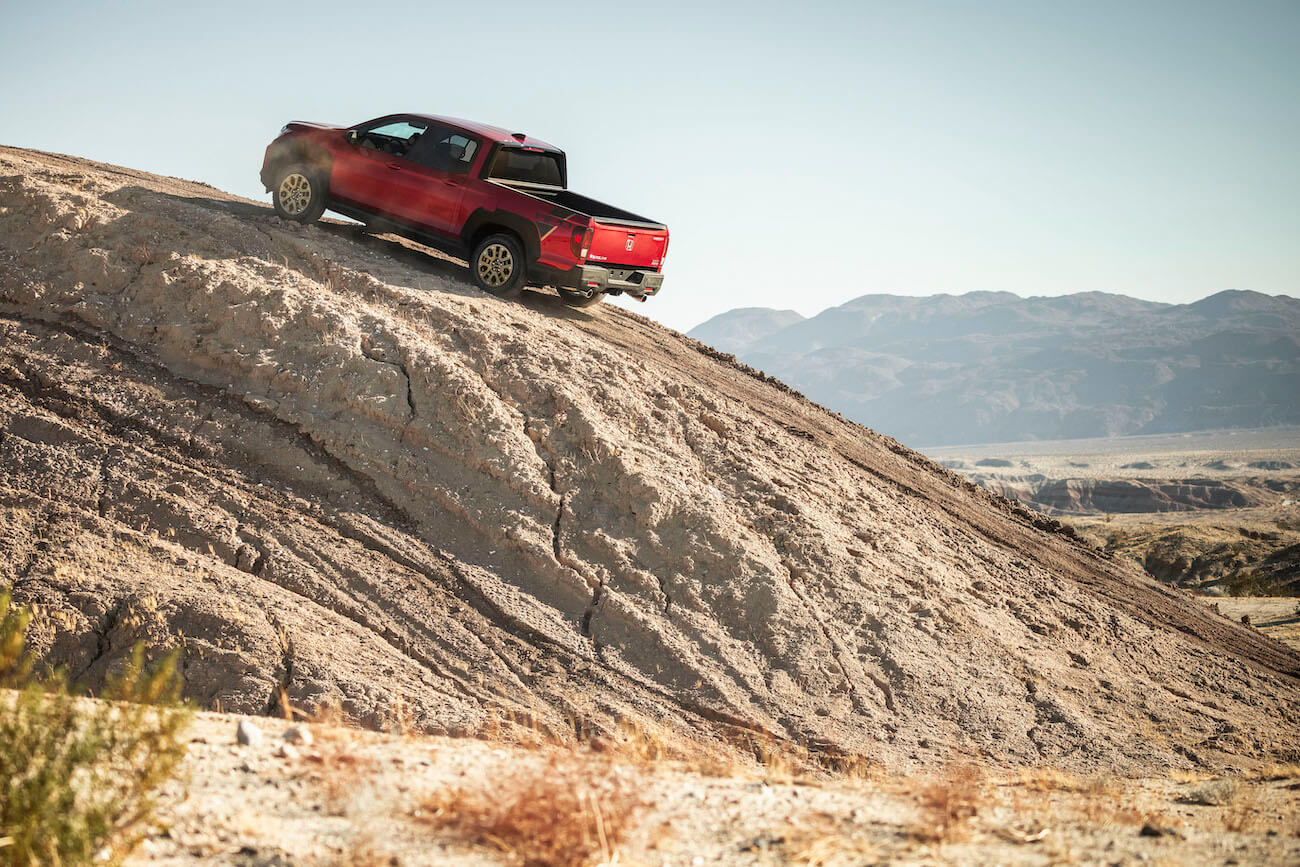 A red 2023 Honda Ridgeline Sport riding up a desert hill.