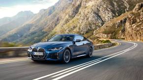 A blue 2024 BMW 4 Series driving down a winding road with cliffs in the background.
