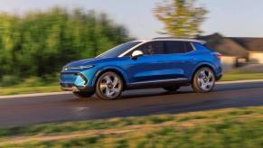 A side profile shot of a blue 2024 Chevy Equinox EV 3LT compact SUV model driving with a blurred background