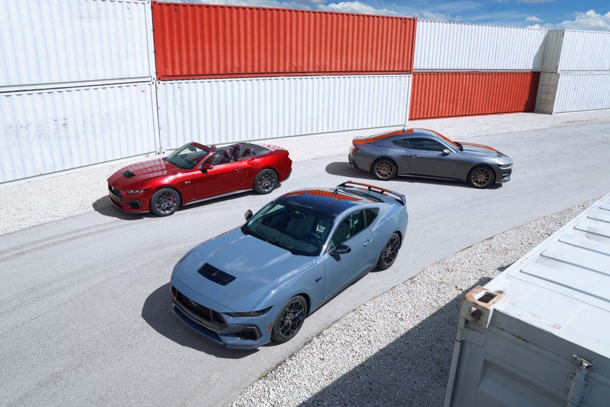 Red, blue, and gray 2024 Ford Mustang coupe and convertible models in front of shipping containers