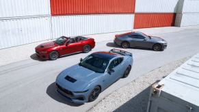 Red, blue, and gray 2024 Ford Mustang coupe and convertible models in front of shipping containers