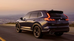 A blue 2024 Honda CR-V Sport Touring, powered by another edition of the classic CR-V engine, driving on the road at sunset.