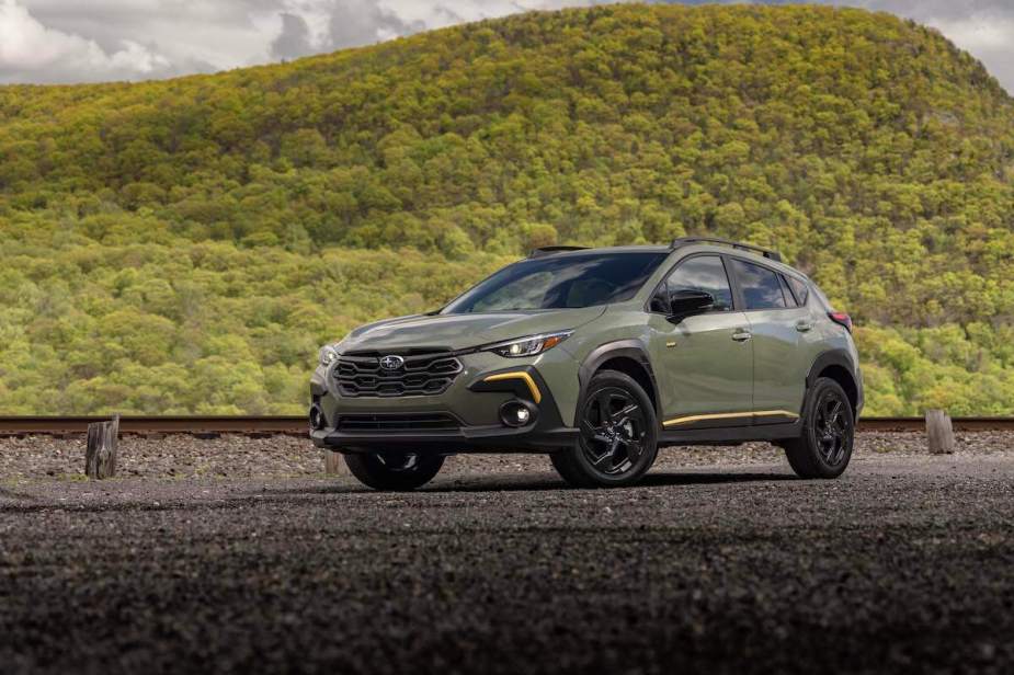 A greenish-gray 2024 Subaru Crosstrek Sport parked in front of a hill covered in green shrubs