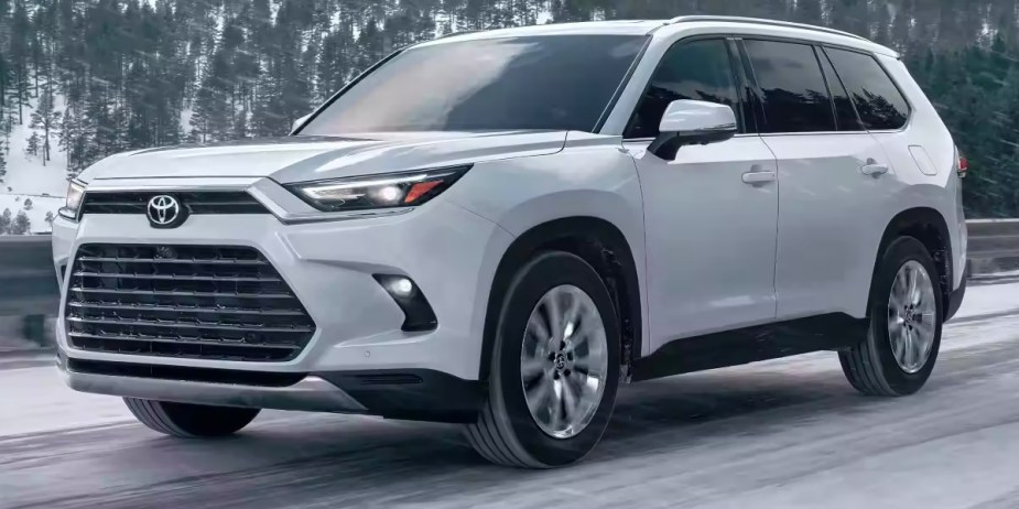 A white 2024 Toyota Grand Highlander is driving on a snowy road. 