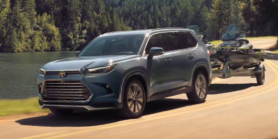 A blue 2024 Toyota Grand Highlander midsize SUV is towing two jet skis on a trailer. 
